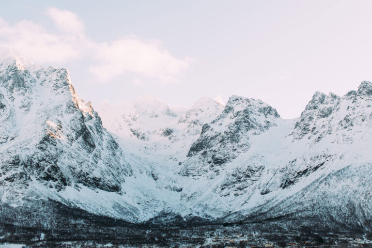 A landscape photograph of the view from the Austnesfjorden rest stop in Norway in the Lofoten islands. Snowcapped mountains surround a small village.