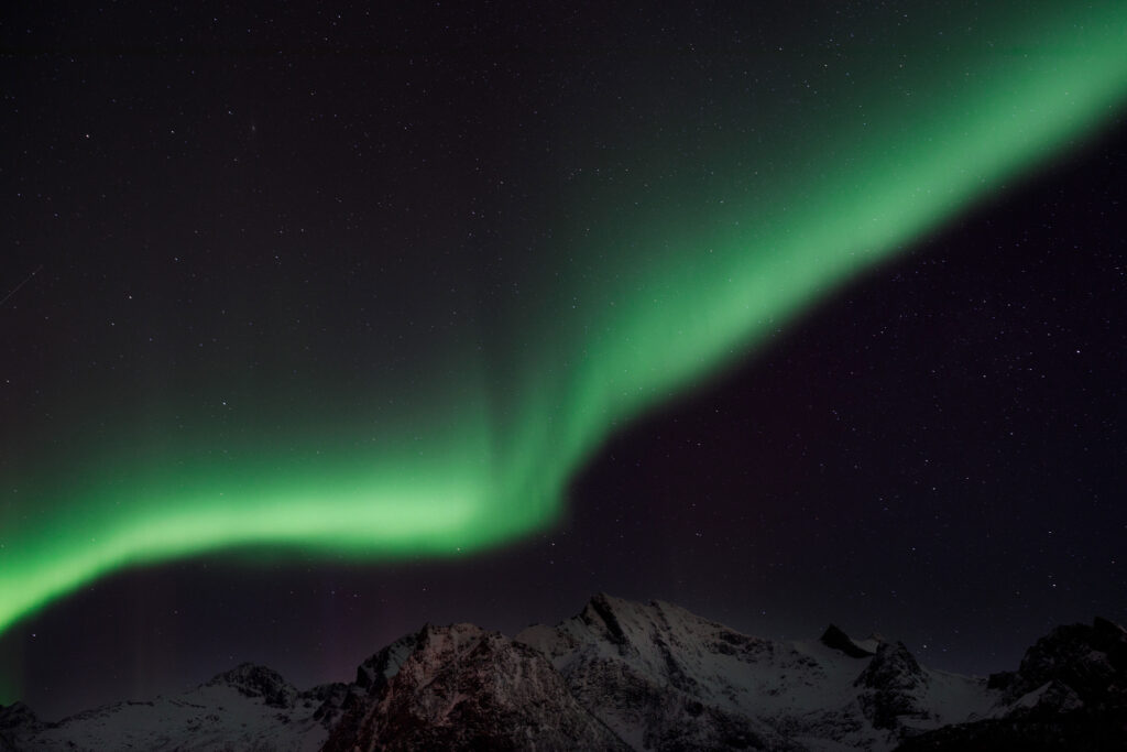 The northern lights are over snow capped mountains